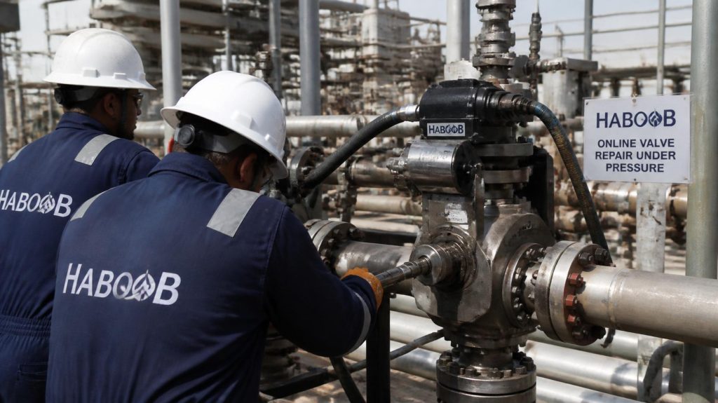 Technicians wearing coveralls with Haboob company name performing online valve repair under pressure at oil and gas plant, hot tapping equipment, live line maintenance, professional photography (2)